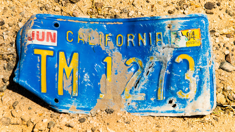 Detail of old damaged car license plate lost in desert yellow sand on Arizona Californian border