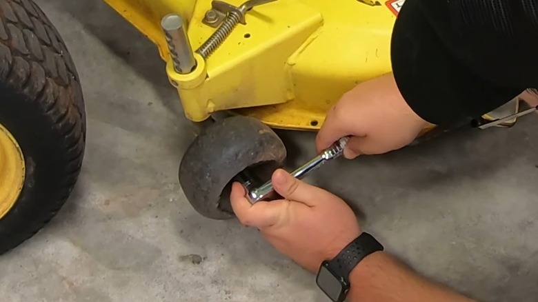 A person removing a mower deck wheel with a socket.