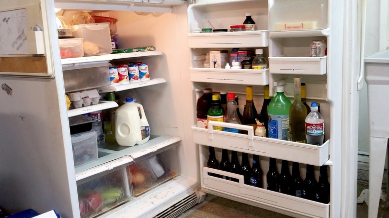 An old, dirty white refrigerator in a garage filled with bottles, eggs, yogurt, milk and more