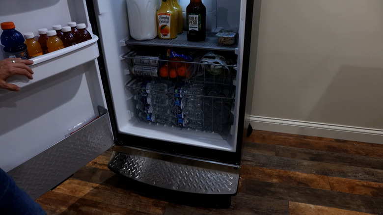 A person loading up a garage-ready refrigerator with various liquid and solid supplies