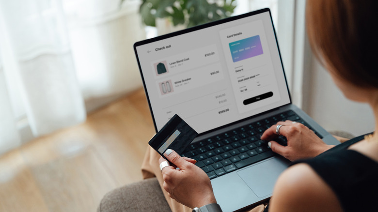 Over the shoulder view of young woman buying clothing online with bank card