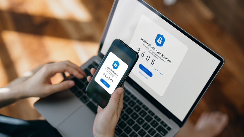 Cropped hand of woman using mobile device with Two-Factor Authentication (2FA) security while logging in securely to her laptop.