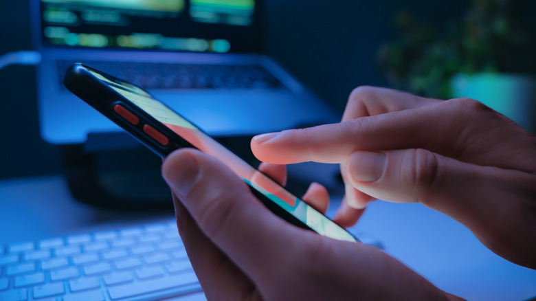 Someone using a smartphone in the foreground with laptop in the background