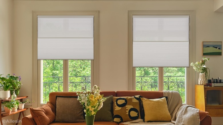 Two windows in living room with shades behind orange couch and flower vase