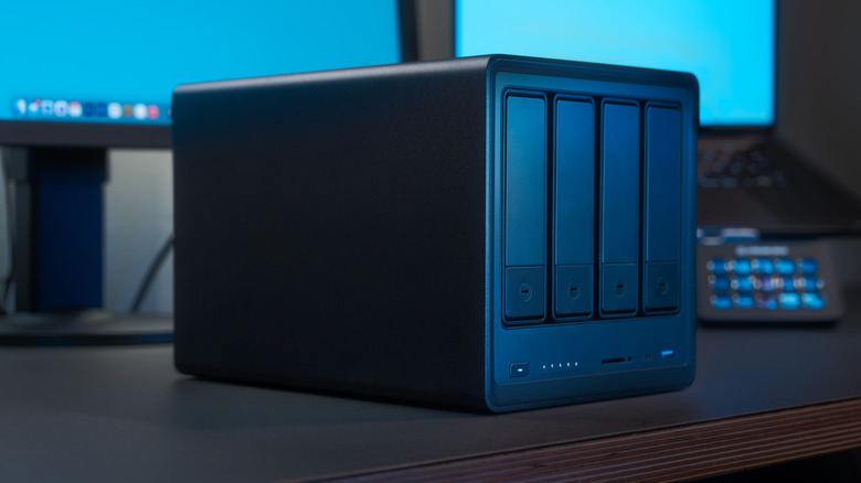 A picture of a black NAS enclosure sitting on a desk, with monitors in the background