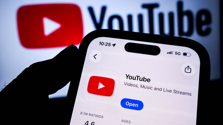 A person holding an iPhone with YouTube app installed on App Store and YouTube banner icon in the background