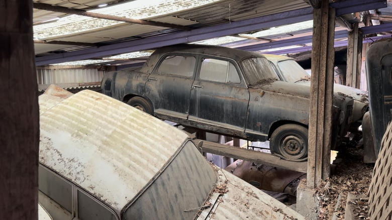 Vintage cars stacked on top of each other in derelict barn.