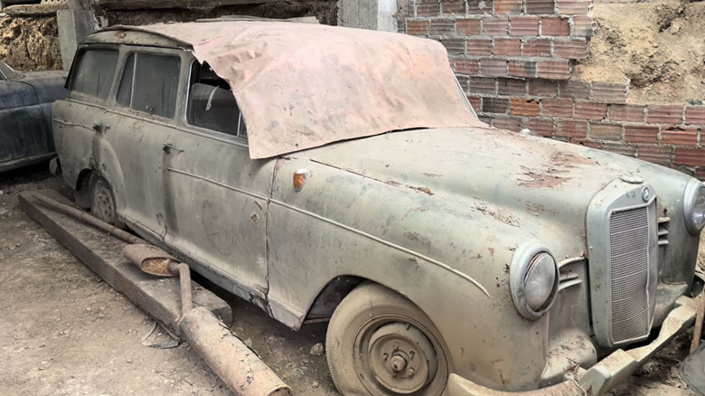 Vintage Mercedes station wagon covered in dust and rust inside of old building.