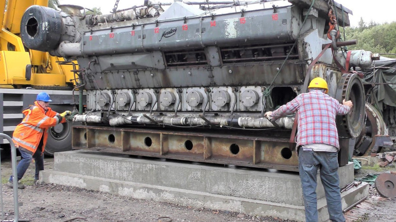 A shot of the massive Mirrlees JV16 engine guided into place on a cement platform