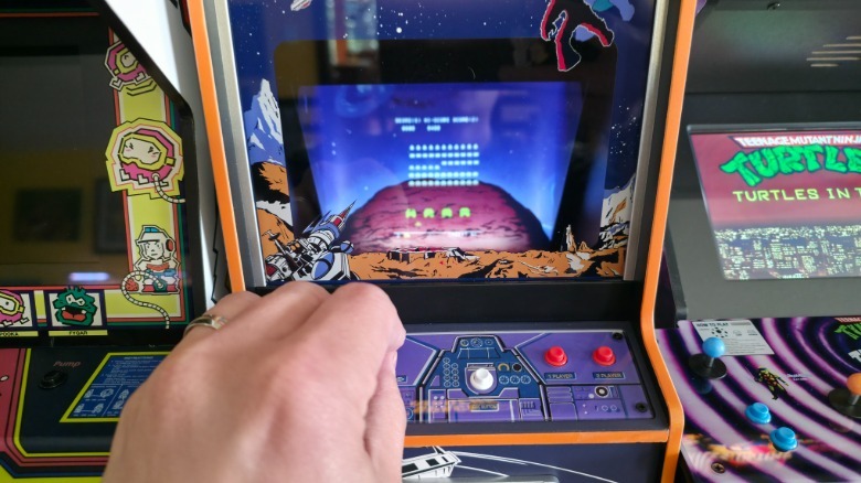 A hand playing with the controls for the Quarter Arcades Space Invaders game