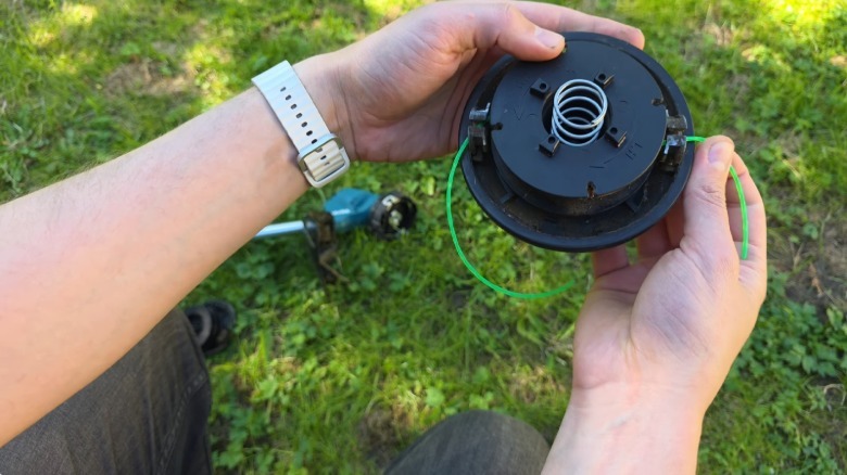 A close up showing a person restringing a Makita string trimmer spool