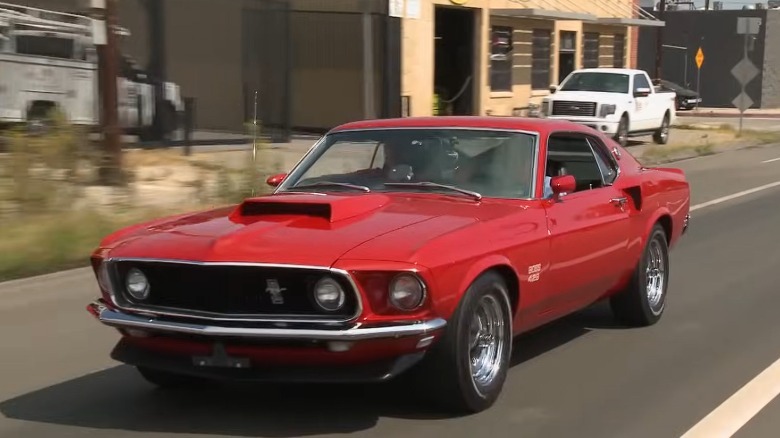 A red 1969 Mustang Boss 429 from Jay Leno's collection being driven down a city street.