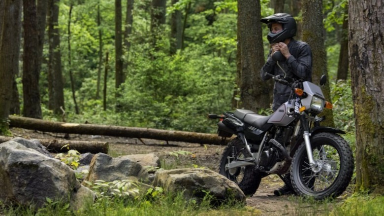 Yamaha TW200 parked in the woods with a rider standing behind it