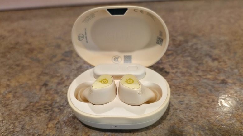 A pair of Arctis GameBuds inside of its open case with the dongle