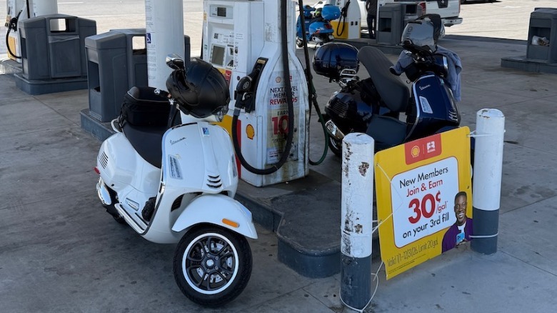 Three Vespa Gts 310 scooters parked at a gas station