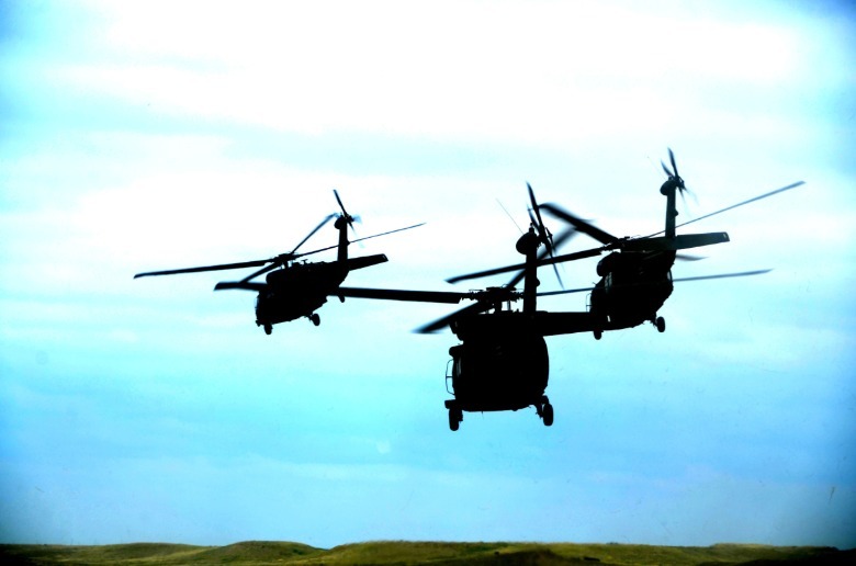 A formation of three Black Hawk helicopters silhouetted against a blue sky.