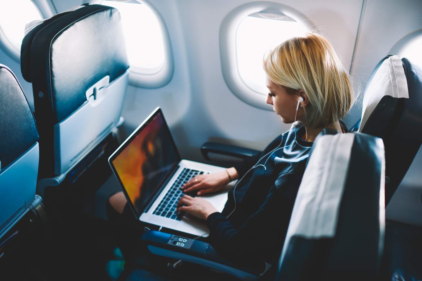 Woman on airplane watches movie on a laptop